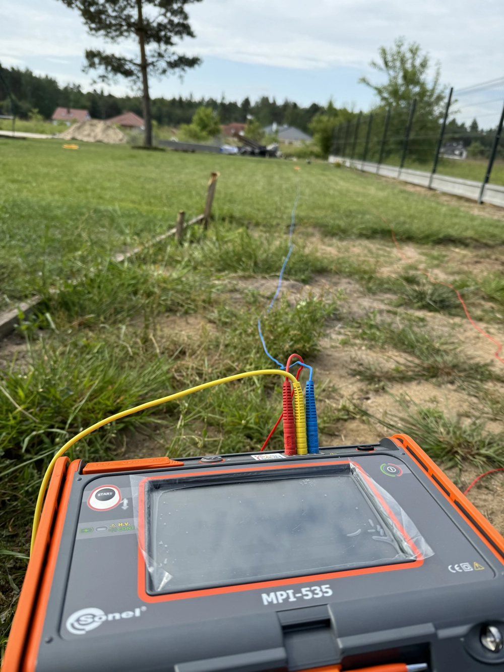 Przenośny miernik podłączony do kabli w trakcie pomiarów instalacji elektrycznych na terenie budowy