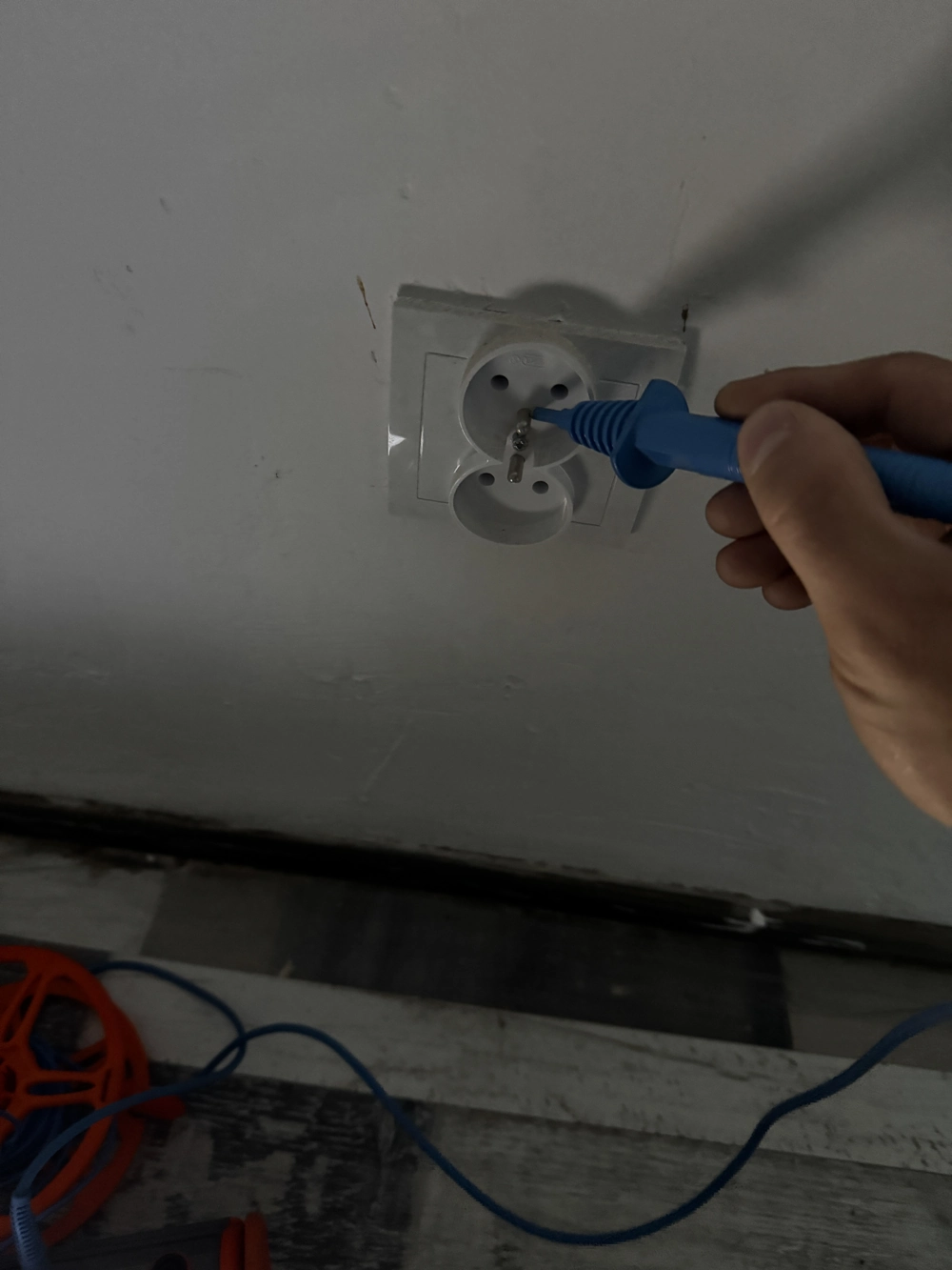 Pomiary instalacji elektrycznych gniazdka – technik trzyma niebieski próbnik przy podwójnym gniazdku na ścianie