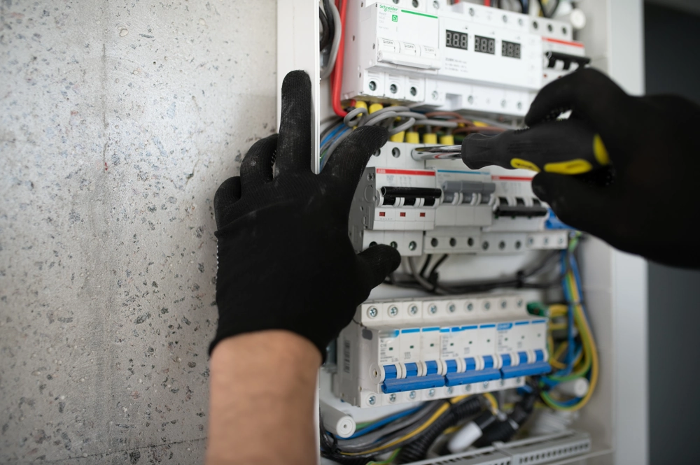 Elektryk w rękawicach dokonuje montażu rozdzielnicy elektrycznej z bezpiecznikami i przewodami