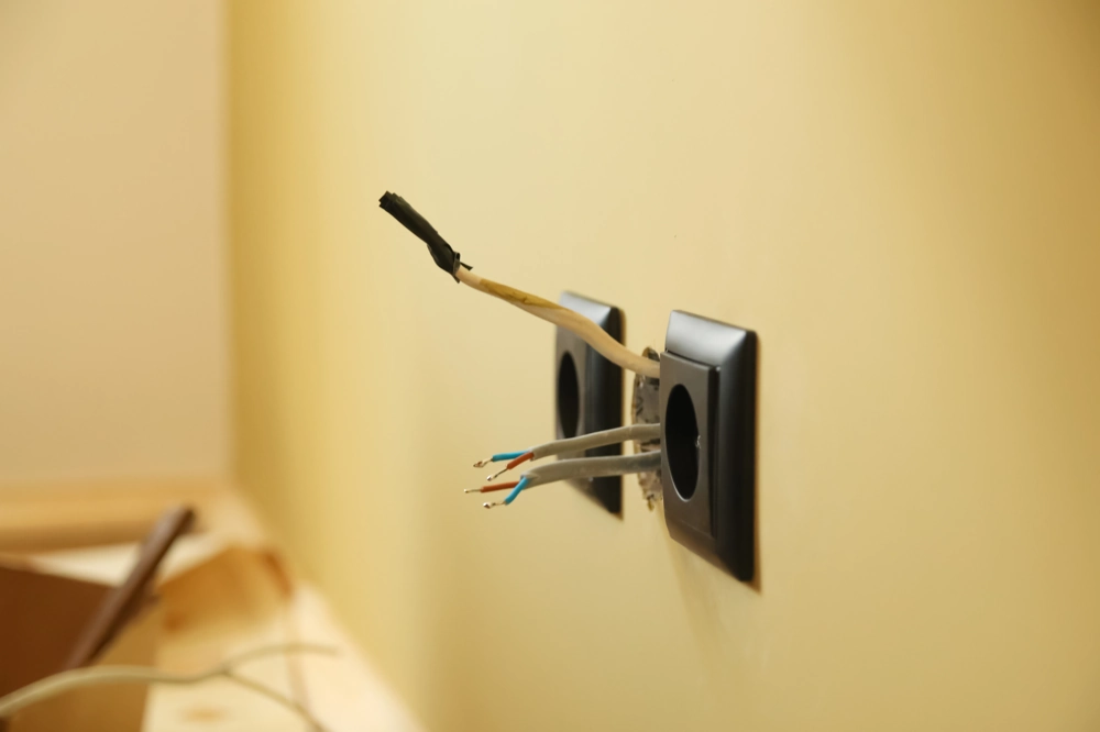 Przewody elektryczne wystające z otworów w ścianie podczas montażu gniazdek