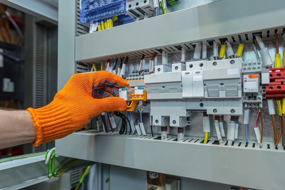 Elektryk w pomarańczowej rękawicy pracuje przy rozdzielnicy w ramach usługi Rozdzielnice elektryczne, precyzyjne podłączenie